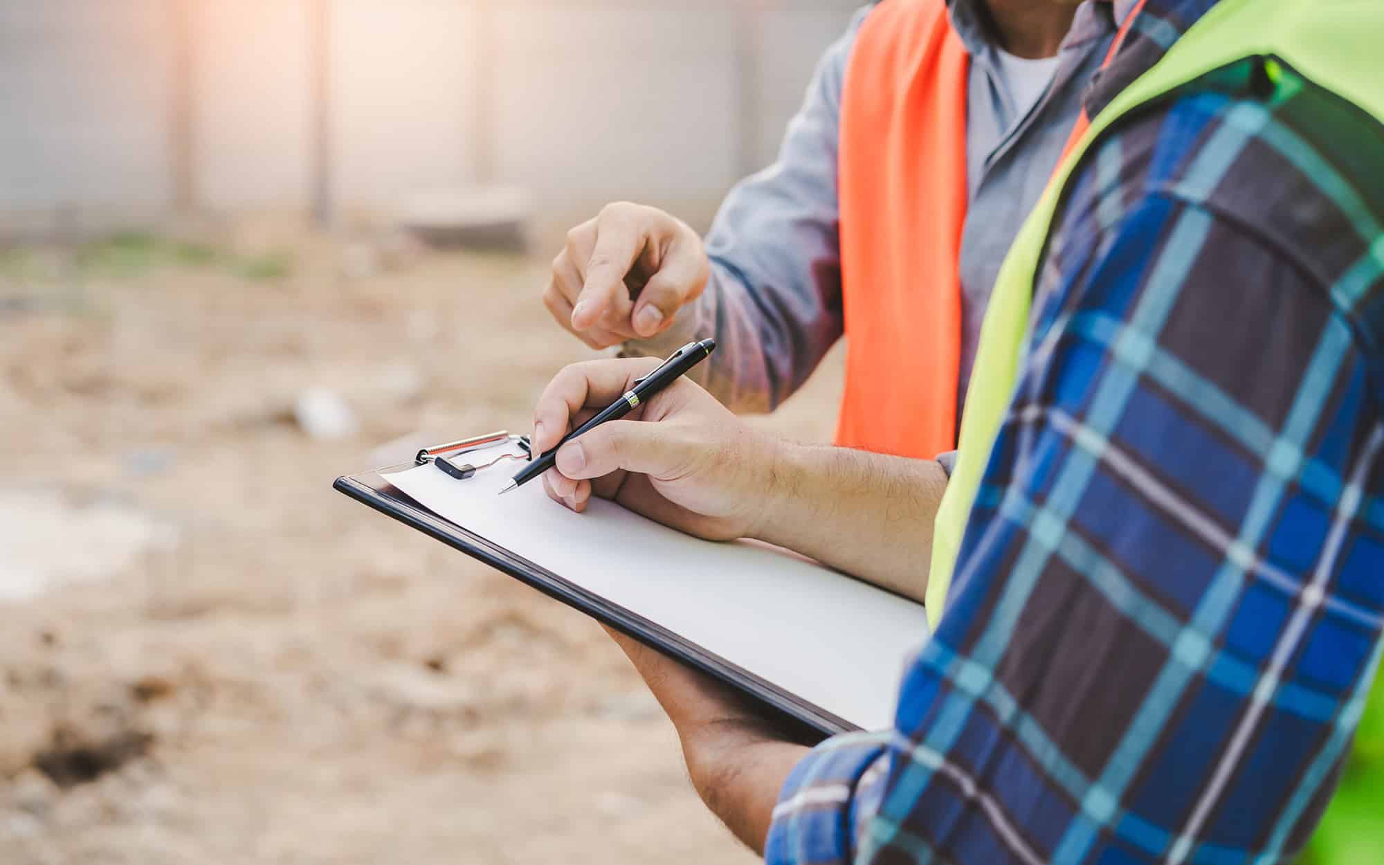 Side view of a construction worker writing something down on clipboard